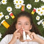 Junge Frau mit Nasenspray liegt auf einer Wiese mit Kamillenblüten und Medikamenten – Symbolbild für Heuschnupfen und Allergiebehandlung